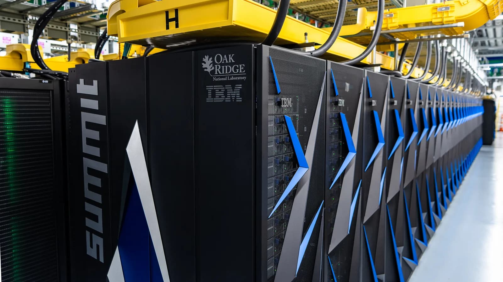 A long row of black supercomputer cabinets in a large computing hall.