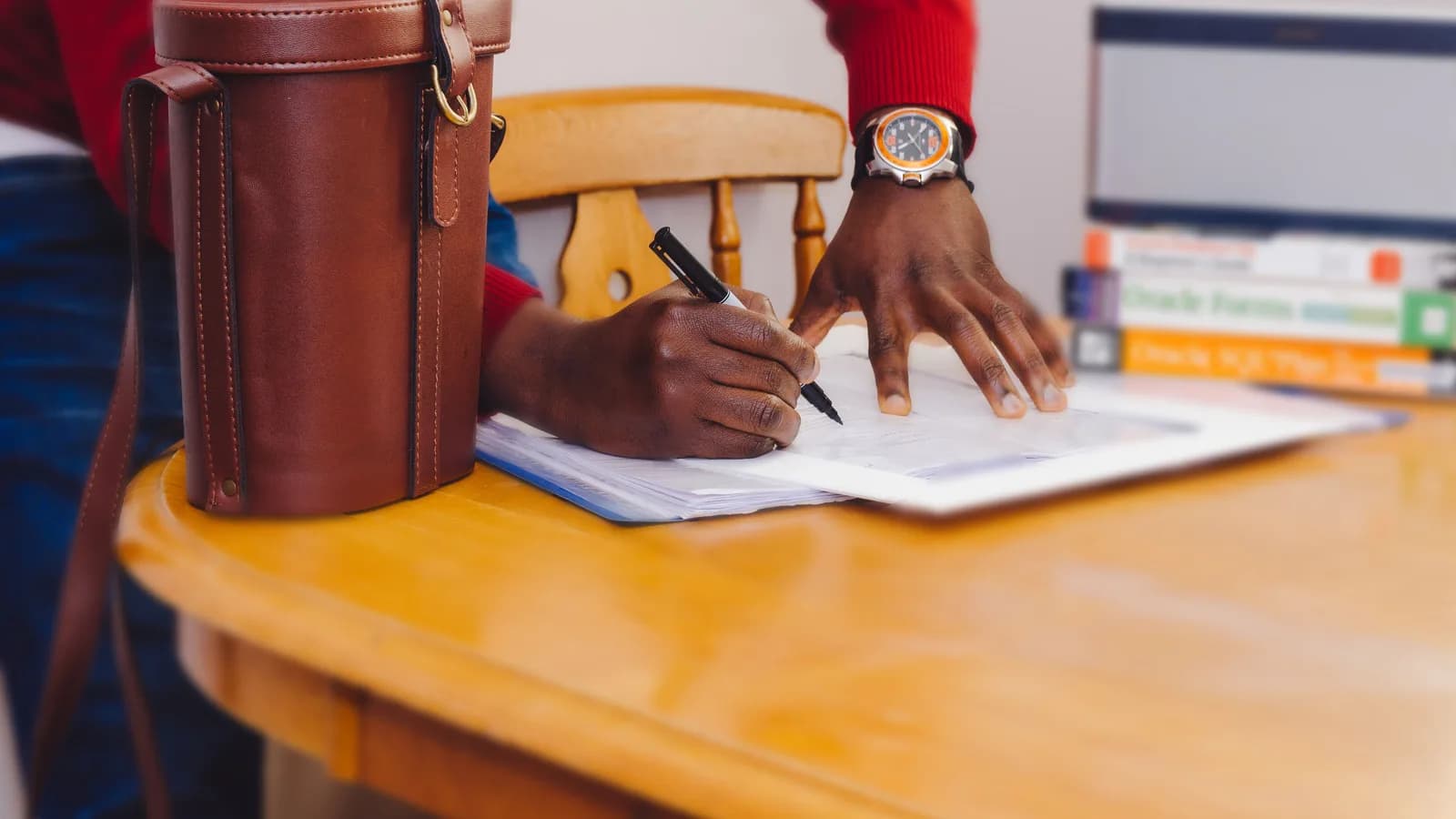 Hands writing notes on paper at a wooden desk.