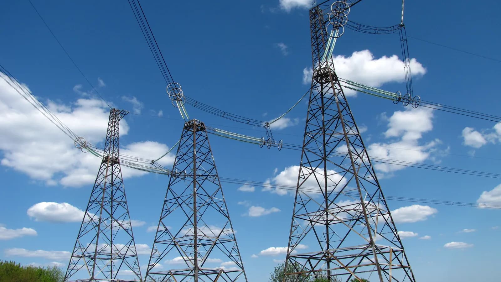 Three steel transmission towers carrying high-voltage power lines under a blue sky.